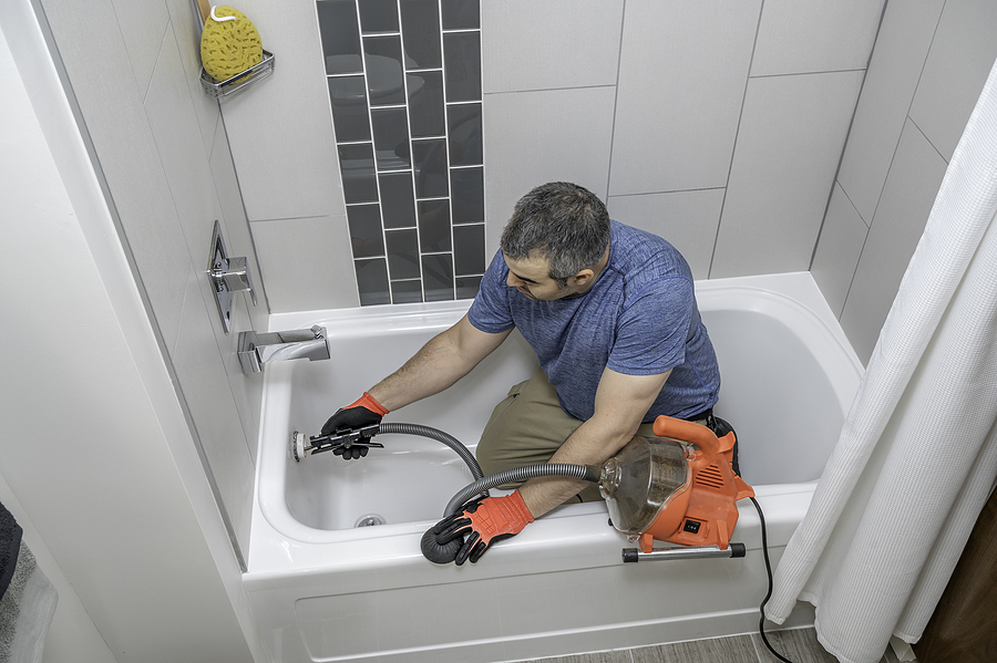 Plumber Drain Cleaning A Bathtub With A Plumbers Snake