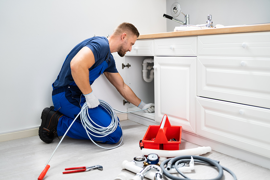 Male Plumber Drain Cleaning a Sink Pipe In Kitchen